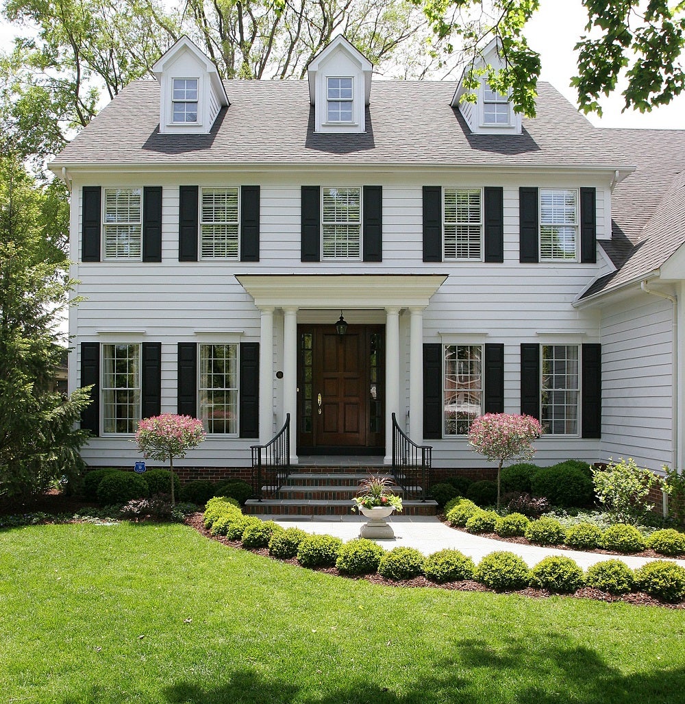 A white colonial home with black shutters and grey shingles 